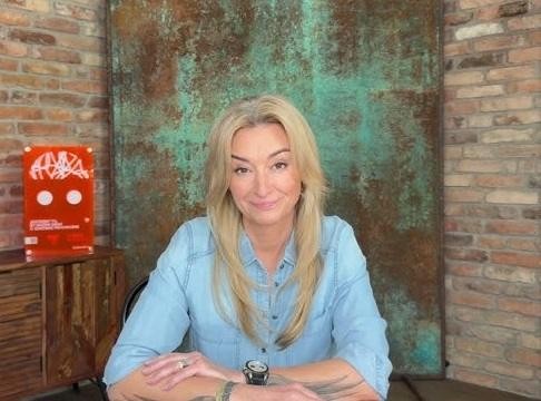 Martyna Wojciechowska w dynamicznej pozie, symbolizującej jej podróżniczą pasję i determinację, z tłem nawiązującym do dalekich wypraw i programu 