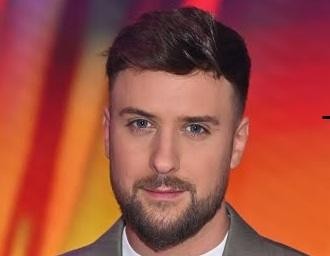 Aleksander Sikora, prezenter telewizyjny, w trakcie dynamicznego prowadzenia programu, z uśmiechem i gestykulacją.
