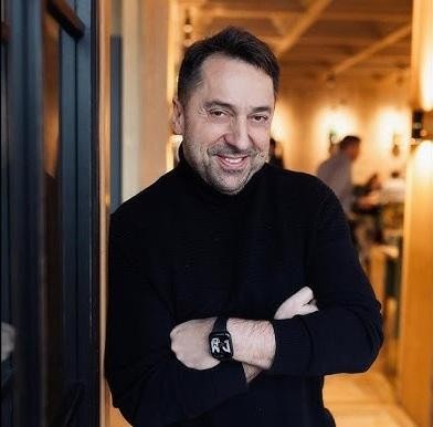 Marcin Miller na scenie, z mikrofonem, śpiewający z pasją, z rozmytym tłem świateł scenicznych i publiczności.