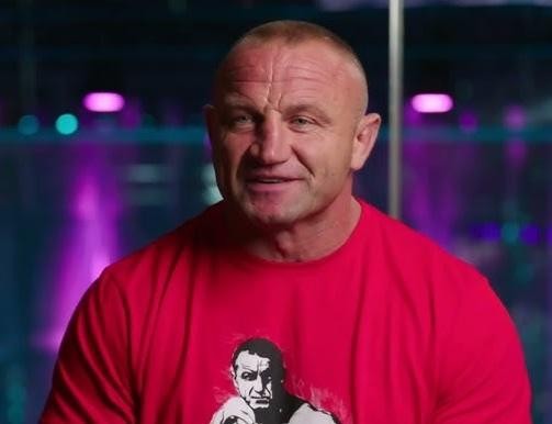 Mariusz Pudzianowski podczas zawodów strongman lub walki MMA, prezentujący swoją siłę i determinację.