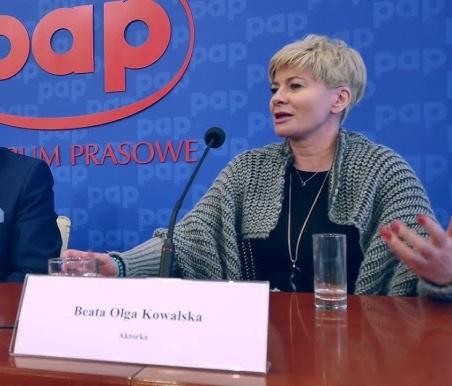Beata Olga Kowalska na planie telewizyjnym, uśmiechnięta i gestykulująca.