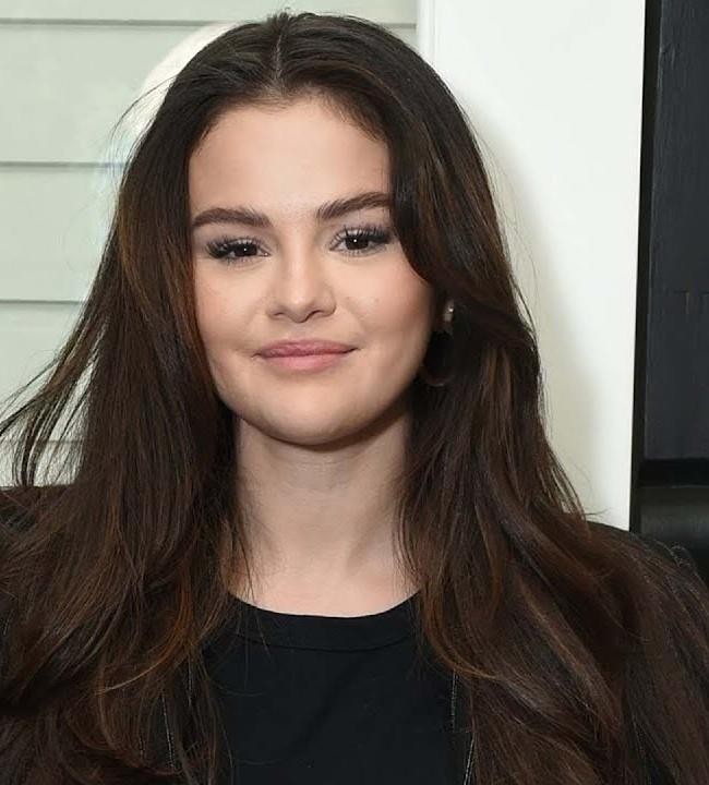 Selena Gomez na scenie podczas koncertu, śpiewająca z pasją, w otoczeniu kolorowych świateł.